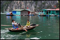 Man holding infant while rowing with feet, Vung Vieng village. Halong Bay, Vietnam (color)
