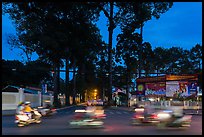 Blurred motorbikes at dusk and tall trees next to Van Hoa Park. Ho Chi Minh City, Vietnam ( color)