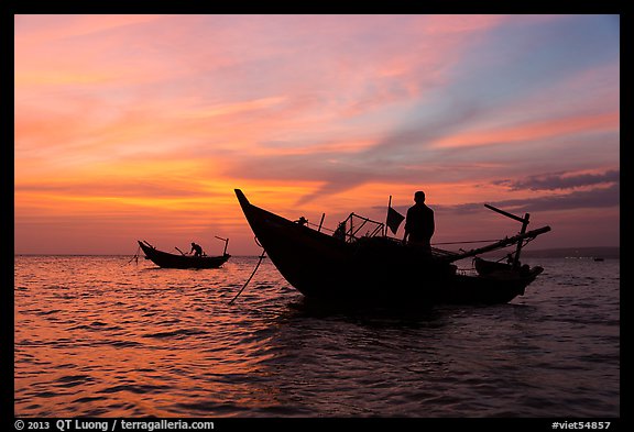 Men on fishing skiffs under bright sunset skies. Mui Ne, Vietnam