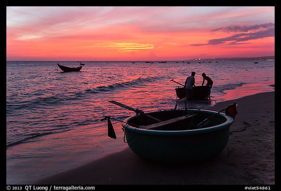Fishermen bringing round coracle boat to shore at sunset. Mui Ne, Vietnam