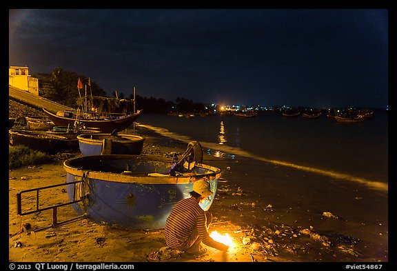 Man with fire next to coracle boat at night. Mui Ne, Vietnam