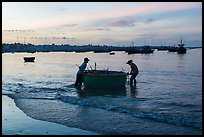 Fishermen pushing coracle boat at dawn. Mui Ne, Vietnam (color)
