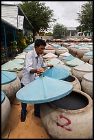Man lifting covers of jars with fermented fish sauce. Mui Ne, Vietnam ( color)