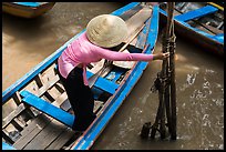 Woman in ao dai reaching to bamboo poles from boat. My Tho, Vietnam (color)