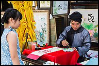 Caligrapher draws Tet greetings as woman looks on. Ho Chi Minh City, Vietnam ( color)