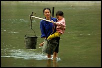 Tay Woman carrying child and water buckets across river. Northeast Vietnam (color)