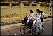 Senior high school girls ride bicycles with impeccable style, wearing elegant Ao Dai uniforms. Ho Chi Minh City, Vietnam ( color)