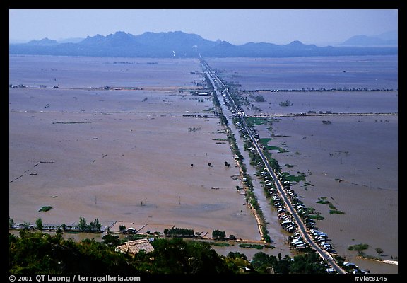 Stilts houses line a road traversing inundated rice fields, seen from Sam mountain. Cambodia is in the far. Chau Doc, Vietnam (color)